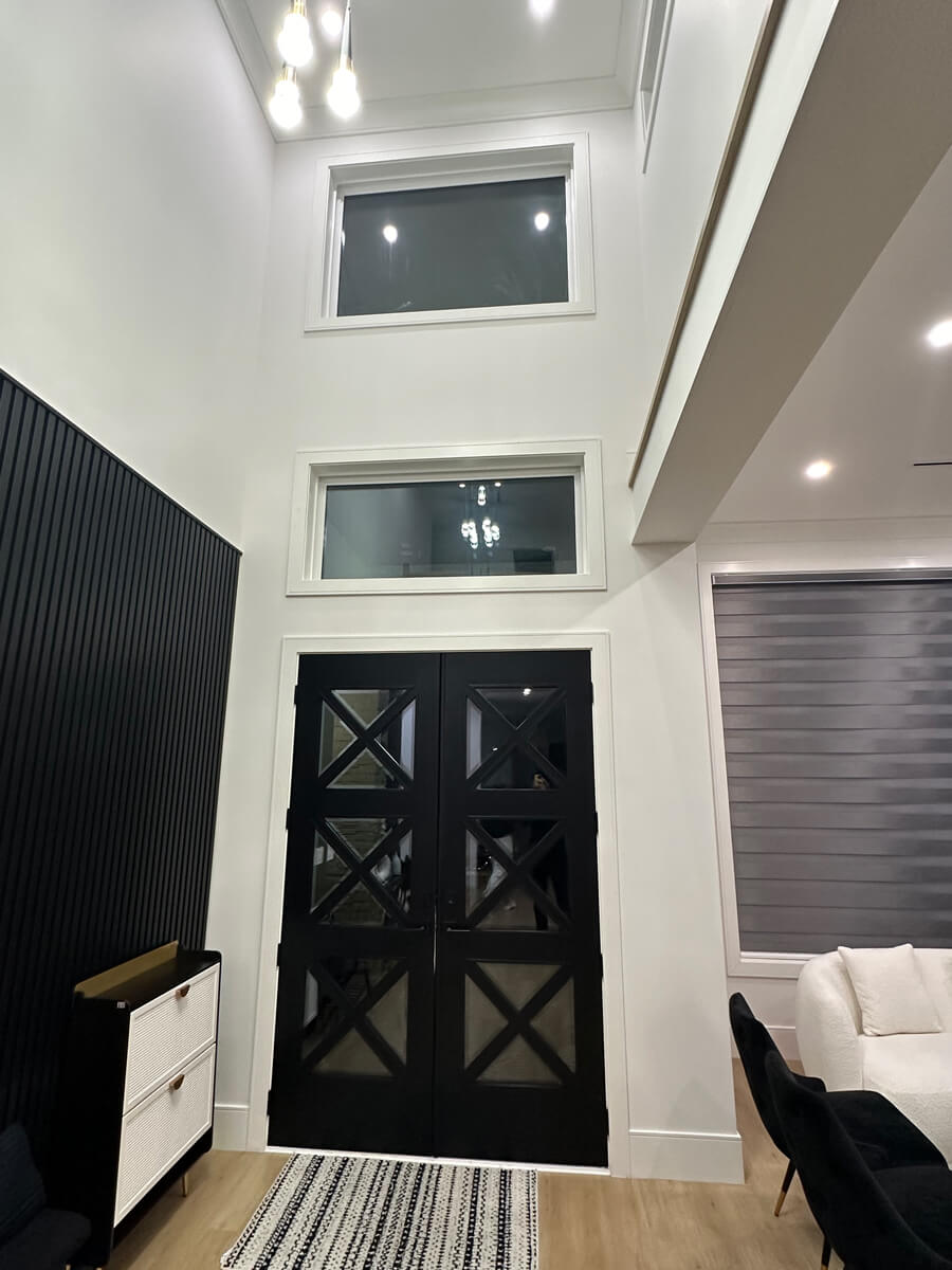 Modern entryway with tall white walls and striking black double doors featuring cross-patterned glass panels.